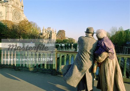France, Paris, elderly couple walking arm in arm on bridge next to Notre Dame Cathedral