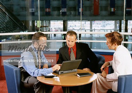Two men and a woman sitting at table, looking at laptop computer