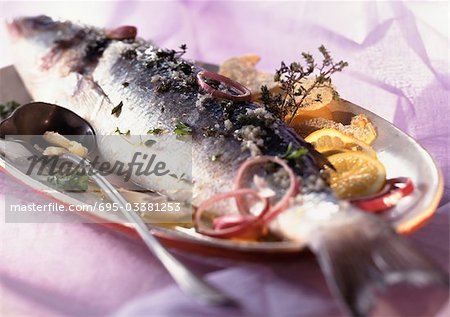 Whole cooked fish with citrus fruit and herbs on dish, close-up