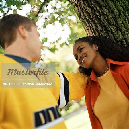 Young woman leaning against tree looking up at young man