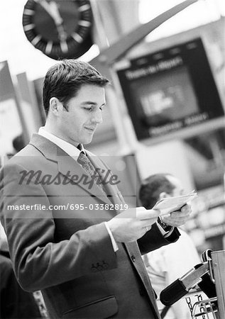 Businessman standing in terminal, looking at tickets, black and white.