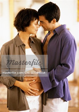 Man hugging pregnant woman, both with hands on her belly, portrait