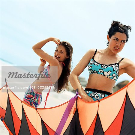 Girl in bathing suit flexing arm muscles, teenager holding kite at the beach
