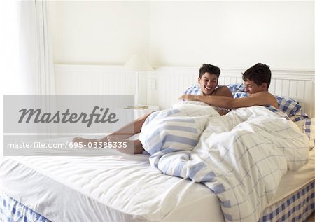 Two teenage boys playfighting in bed