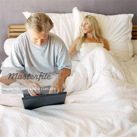 Couple in bed, man using laptop