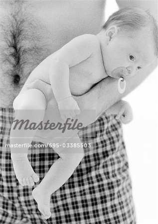 Father holding infant with pacifier in mouth, b&w