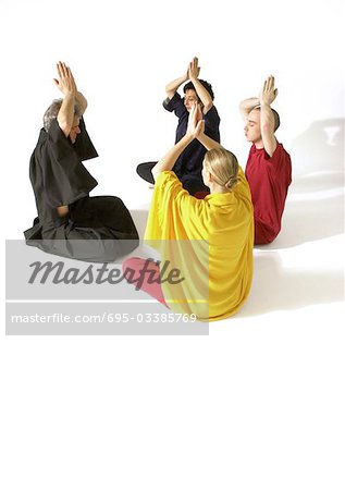 Group of people sitting on floor indian style, meditating with hands togther over heads