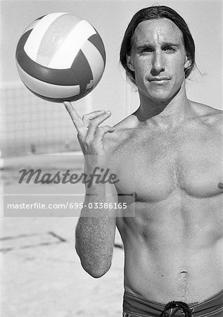 Young bare-chested man, holding volleyball on finger, portait, b&w.