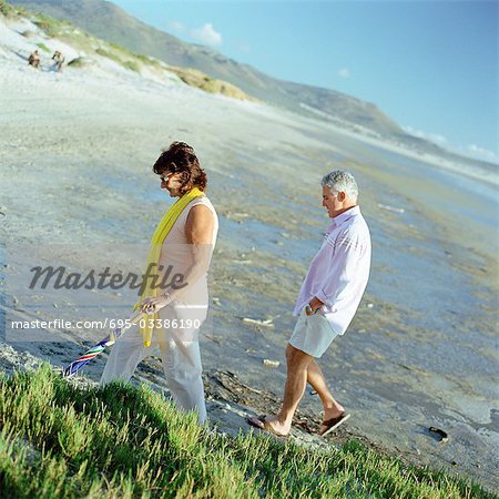 Mature couple walking on beach, side view