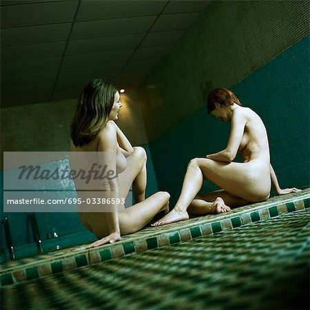 Two mid-adult women friends at spa together, sitting nude by side of pool - Stock Photo - Masterfile