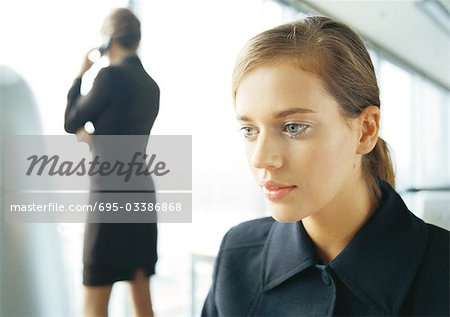 Businesswoman on cell phone, rear view, in background, blurred, businesswoman working in foreground, close-up