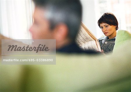 Businessman and businesswoman reading newspaper, blurred foreground