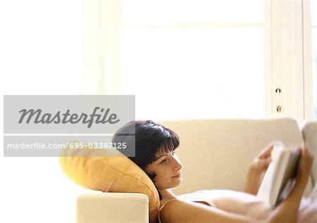 Woman lying back on sofa, reading