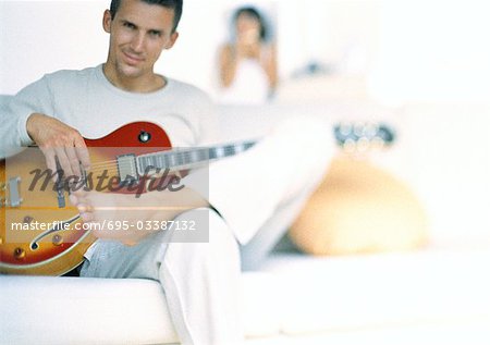 Man playing guitar, woman blurred in background