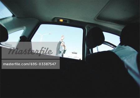 Businessman seen through taxi car window waving hand, hailing taxi car.