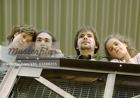 Four young friends standing next to rail, low angle view