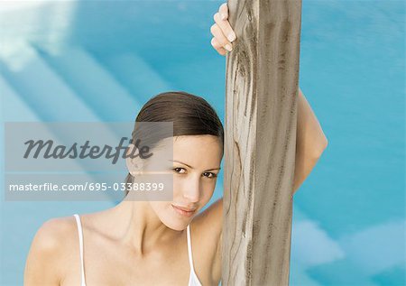 Woman standing by pool, leaning against wooden pole