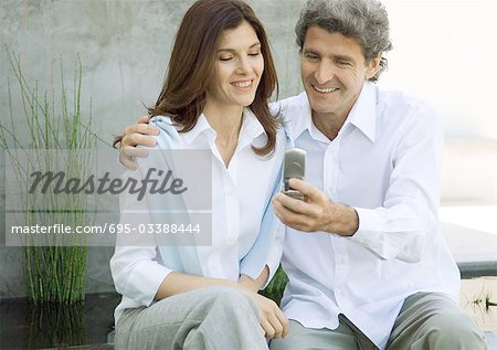 Mid-adult couple, man showing woman cell phone