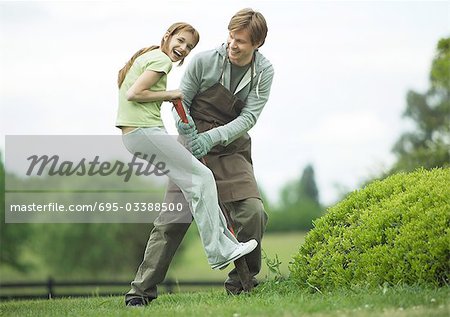 Girl standing on shovel, laughing, while young man holds shovel