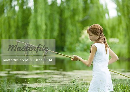Girl holding stick with algae hanging from it, pond in background