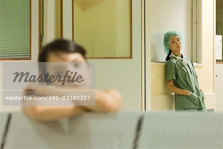 Female surgeon standing with hands in pockets, looking at camera, woman resting head on arms in foreground