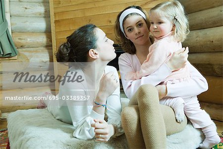 Two teenage girls sitting on bed, one holding toddler on lap