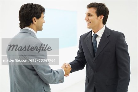 Two businessmen shaking hands, smiling at each other, side view