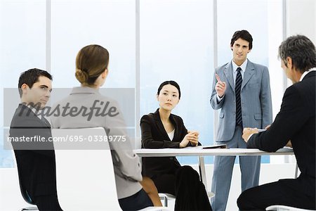 Business associates having meeting, one standing, pointing