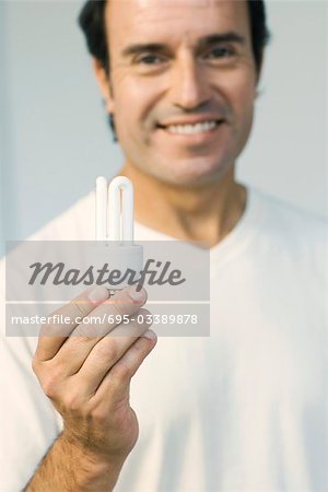 Man holding energy efficient light bulb, smiling at camera