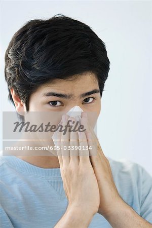 Young man blowing his nose, looking at camera