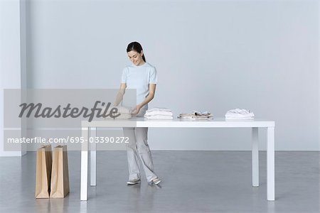 Woman standing at table, looking at folded sweater