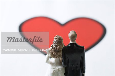 Miniature Bride And Groom Standing In Front Of Large Heart Graphic