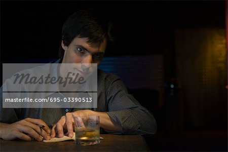 Man sitting in bar with pen, notebook and glass of whiskey, looking at camera