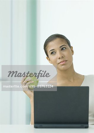 Woman holding apple, sitting at laptop