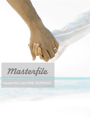 Married couple holding hands on beach, close-up of hands