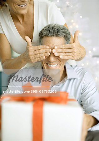 Woman covering man's eyes before giving him christmas gift