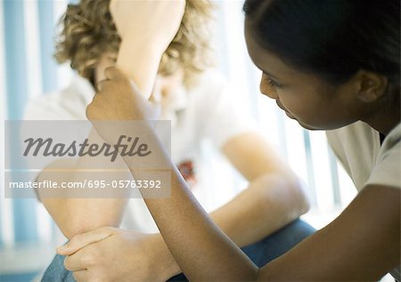 Teen boy sitting with head down, teen girl talking to him