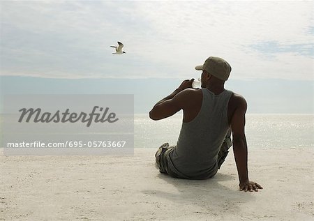 https://image1.masterfile.com/getImage/695-05763667em-man-drinking-water-on-beach-stock-photo.jpg