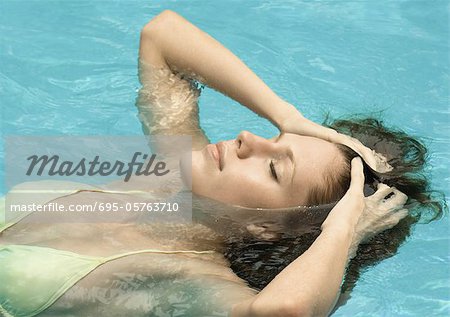 Woman in pool, head back and hands in hair with eyes closed