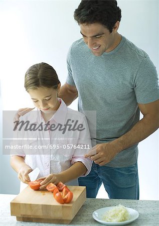 Man standing behind daughter as she cuts up tomatoes