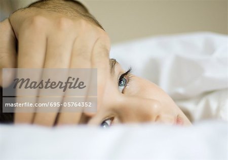 Child lying in bed with father's hand on forehead