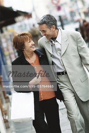 Mature couple walking on city sidewalk, smiling at each other