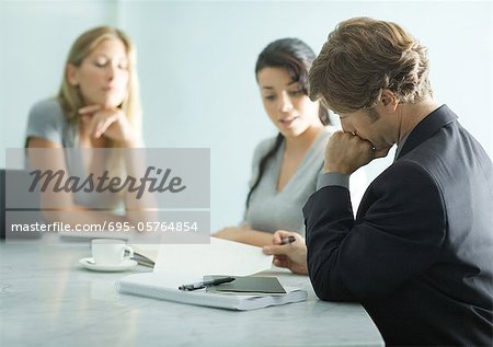 Mature man sitting at table with teenage girl and young female professional, reading document