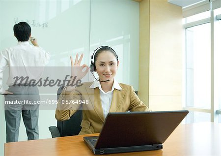 Businesswoman wearing headset and using laptop, making ok gesture