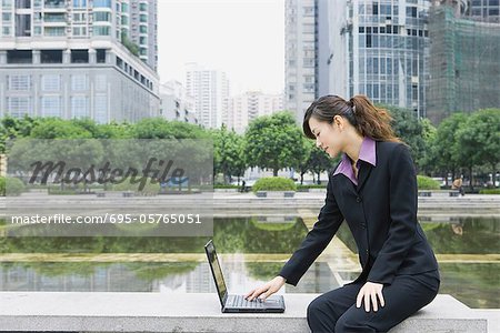 Businesswoman using laptop by water in office park