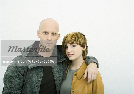 Young adult couple looking at camera, man with arm around woman, portrait