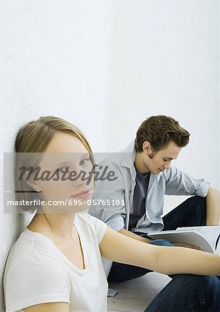 Teenage girl and young man sitting on floor, girl looking at camera