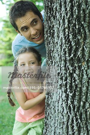 Girl and father peeking around tree