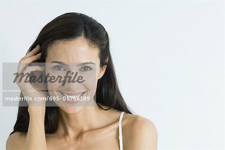 Woman, pushing hair back, smiling at camera, portrait