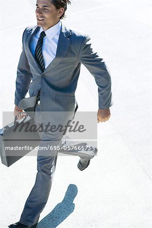 Young businessman running outdoors, carrying briefcase